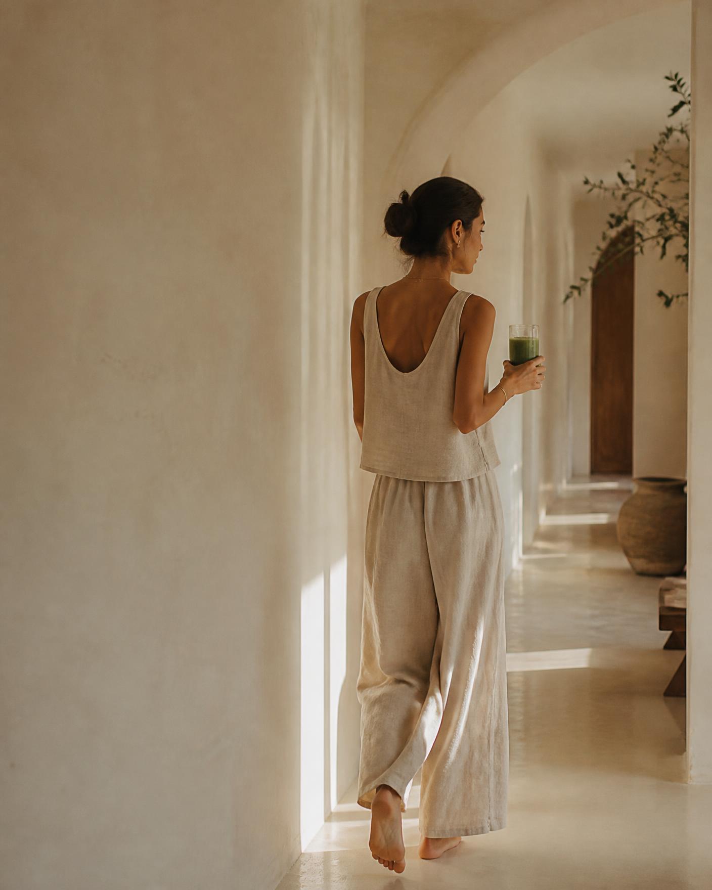 Mujer en un pasillo luminoso con un batido verde, estética wellness editorial